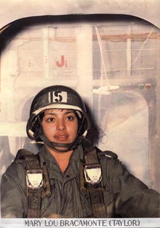 Woman in flight suit and a helmet seated in an aircraft.