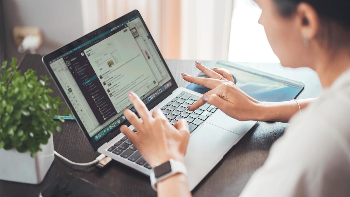 Person typing on a laptop computer at a brown table with a green plant on it.